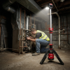 Technician using Milwaukee M12 cordless tripod stand light while servicing boiler in dark basement